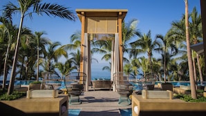 Een zwembadcomplex van een resort met uitzicht op de oceaan, met ligbedden en een pergola.