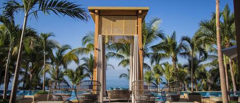 A resort pool area with a view of the ocean, featuring lounge chairs and a pergola.
