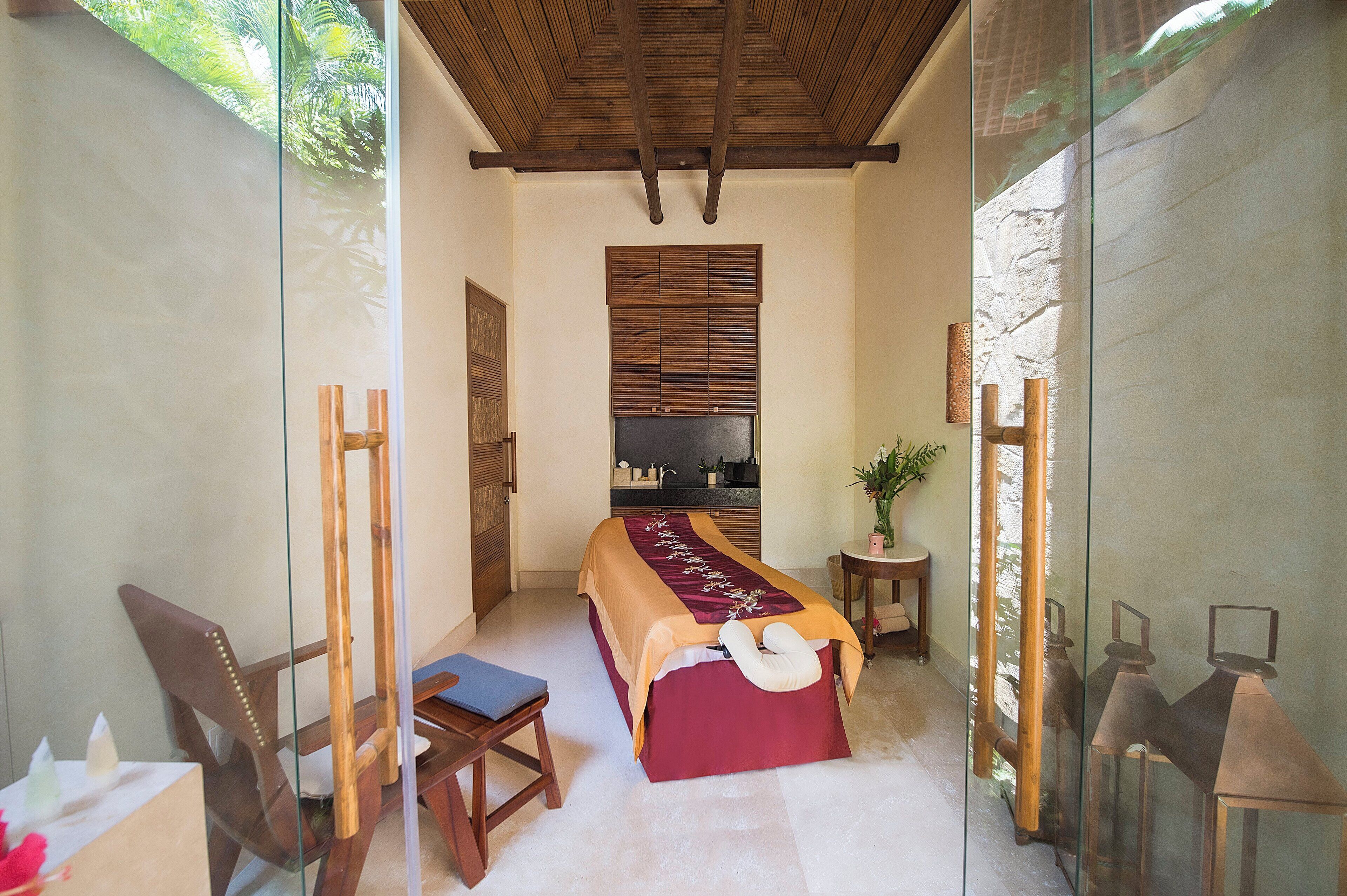 Una habitació amb un llit, una cadira, una taula petita i una separació de vidre.