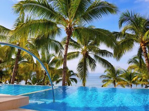 Una piscina azul cristalina rodeada de palmeras, con vista al océano en el fondo.
