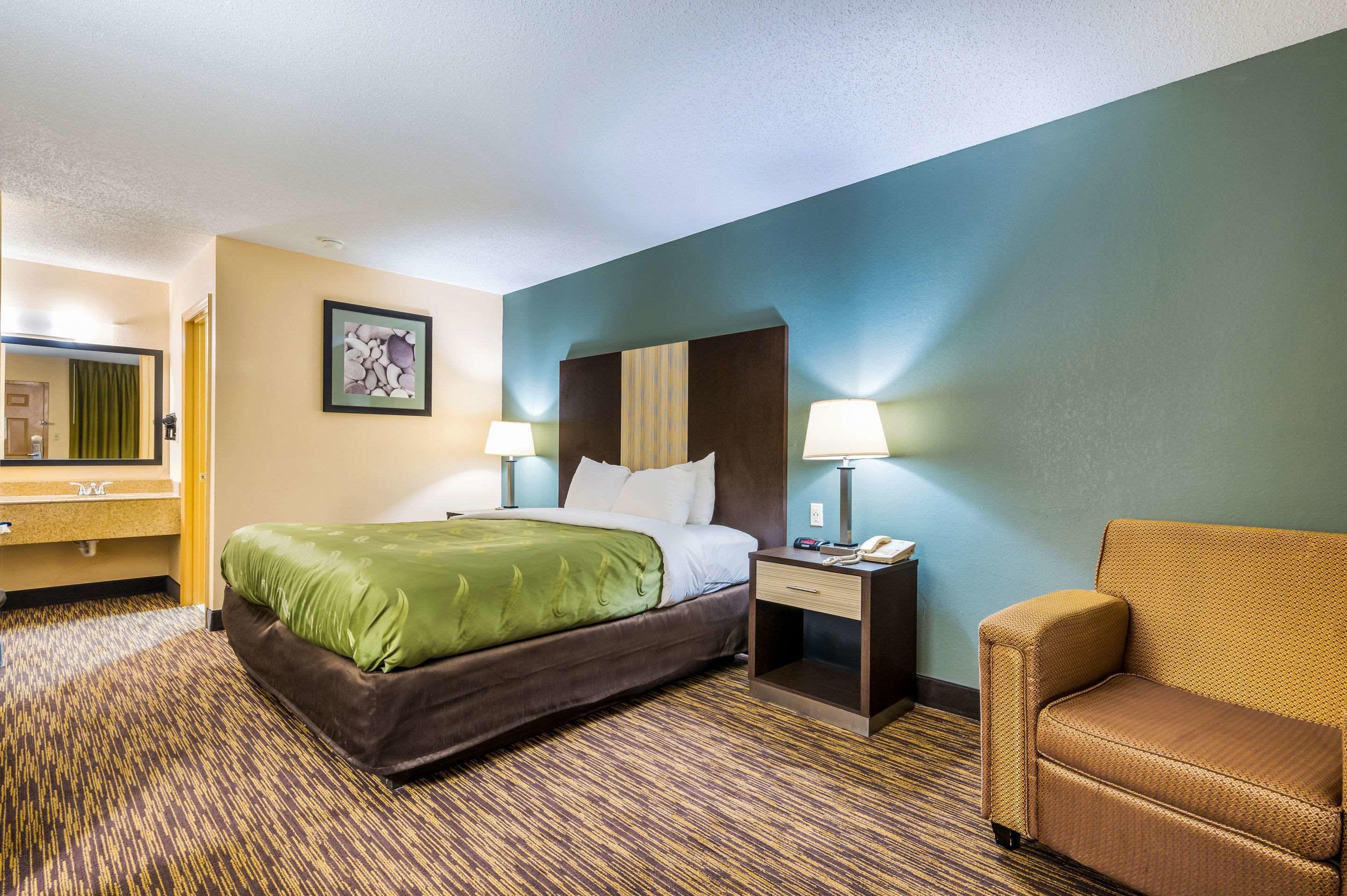 Une chambre d’hôtel avec un lit, deux tables de chevet avec des lampes, une chaise, un miroir et un tableau au mur.