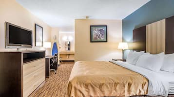 A hotel room with a large bed, a desk with a chair, a television, and a framed picture on the wall.