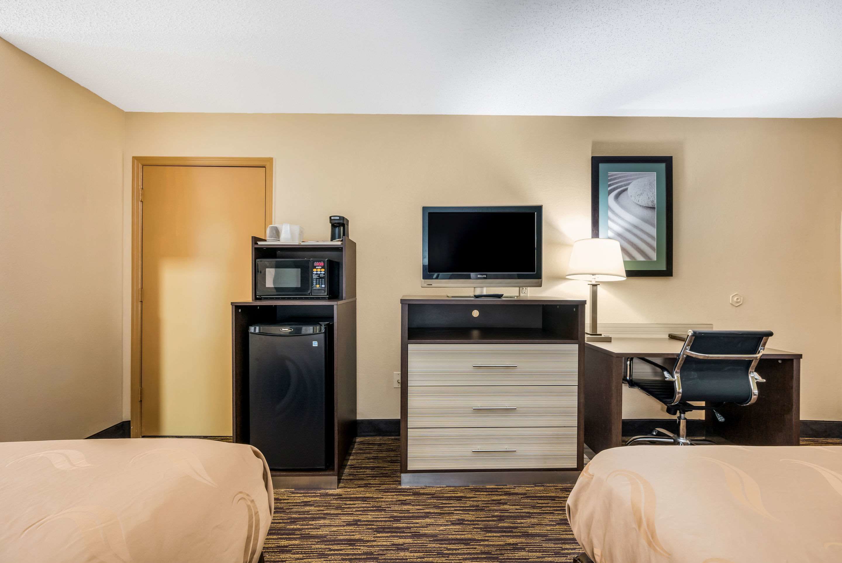 A hotel room with two beds, a desk with a chair, a television, a microwave, and a refrigerator.