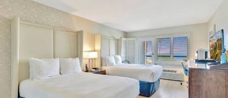 A hotel room with two beds, a desk, and a view of the outside.
