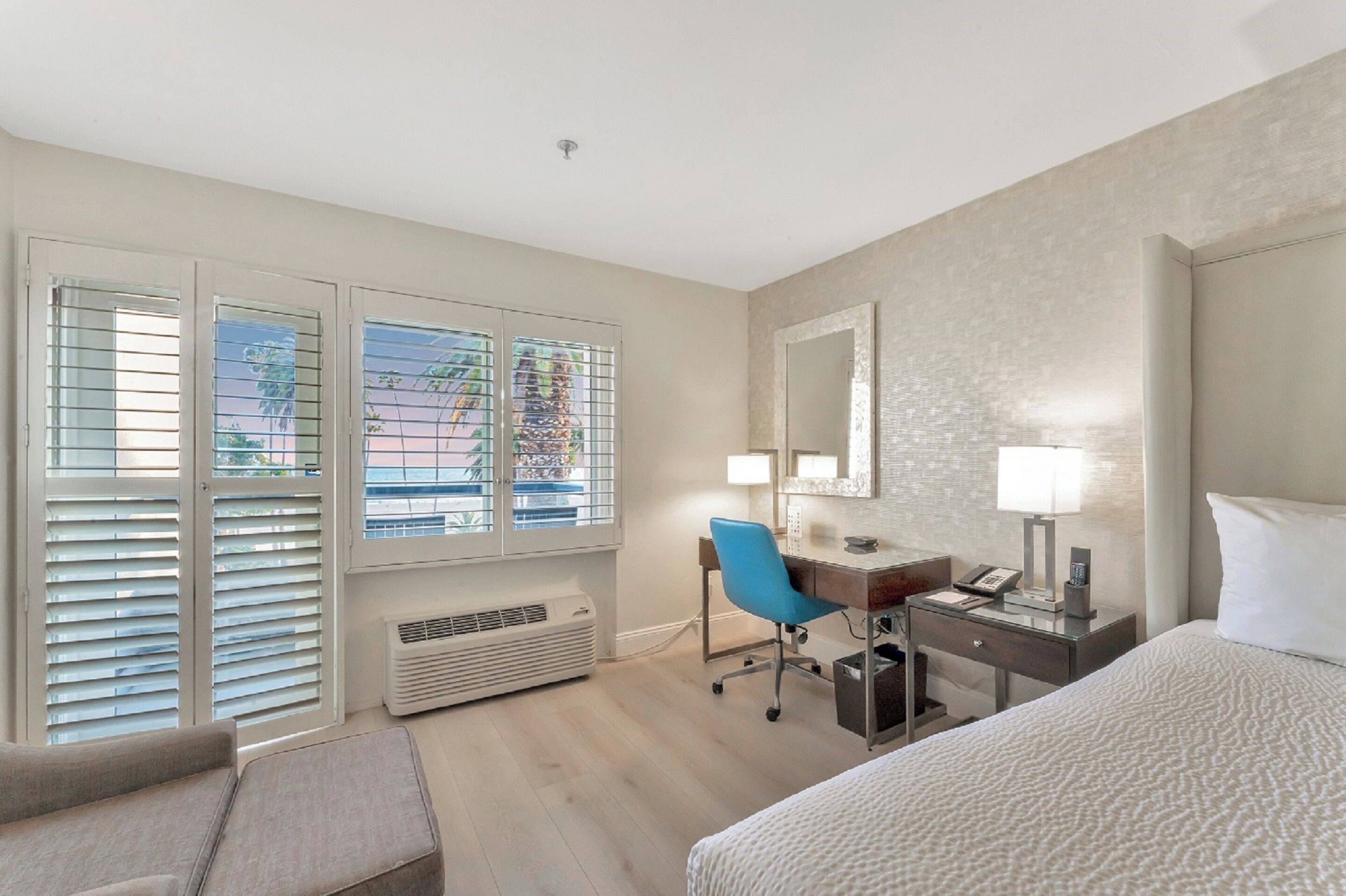 Quarto de hotel com cama, escrivaninha, cadeira e janela com persianas.