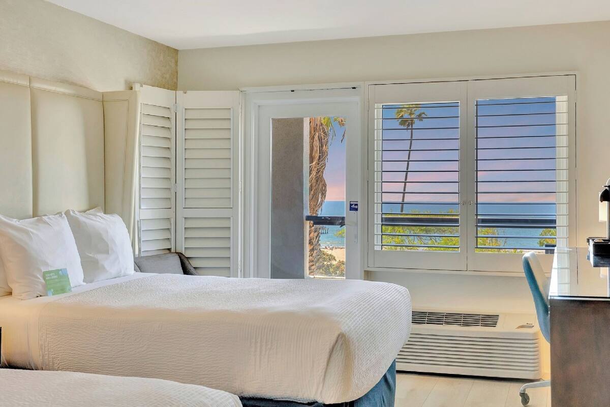 A hotel room with a bed, a desk, and a view of the beach through the window.