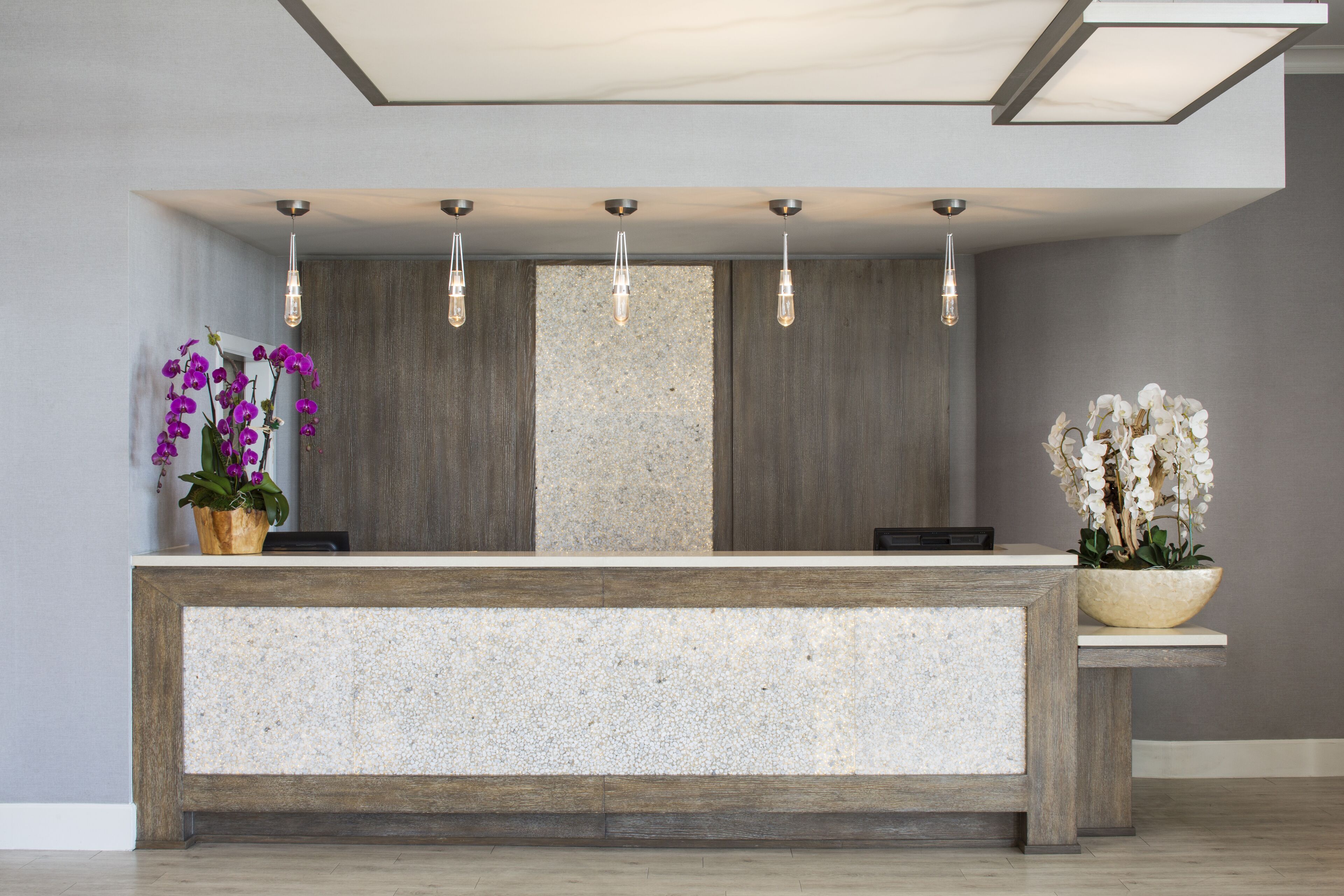 A reception desk with a stone top, wooden paneling, and hanging pendant lights.