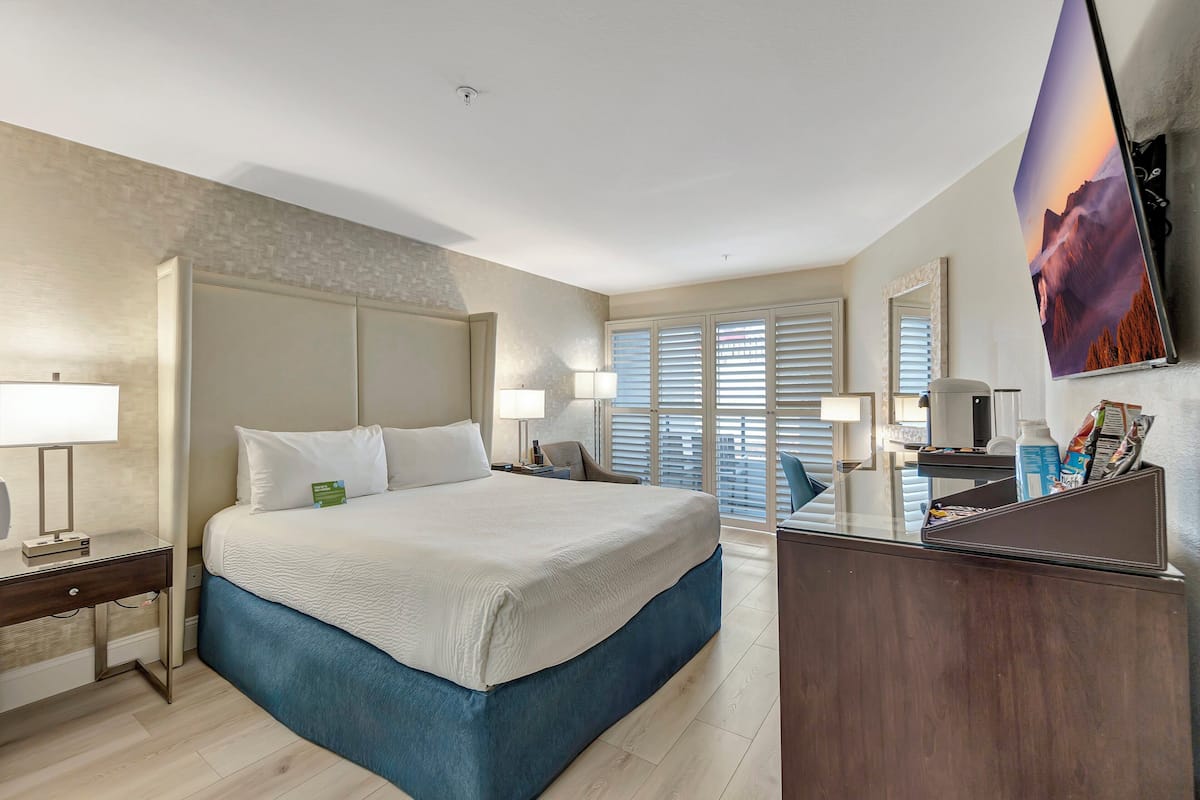 A modern hotel room with a large bed, a desk, and a flat-screen TV mounted on the wall.