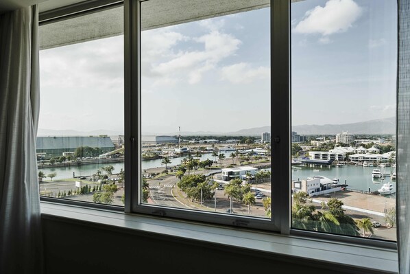 Vista desde una ventana sobre un puerto deportivo con barcos, un río y montañas a lo lejos.