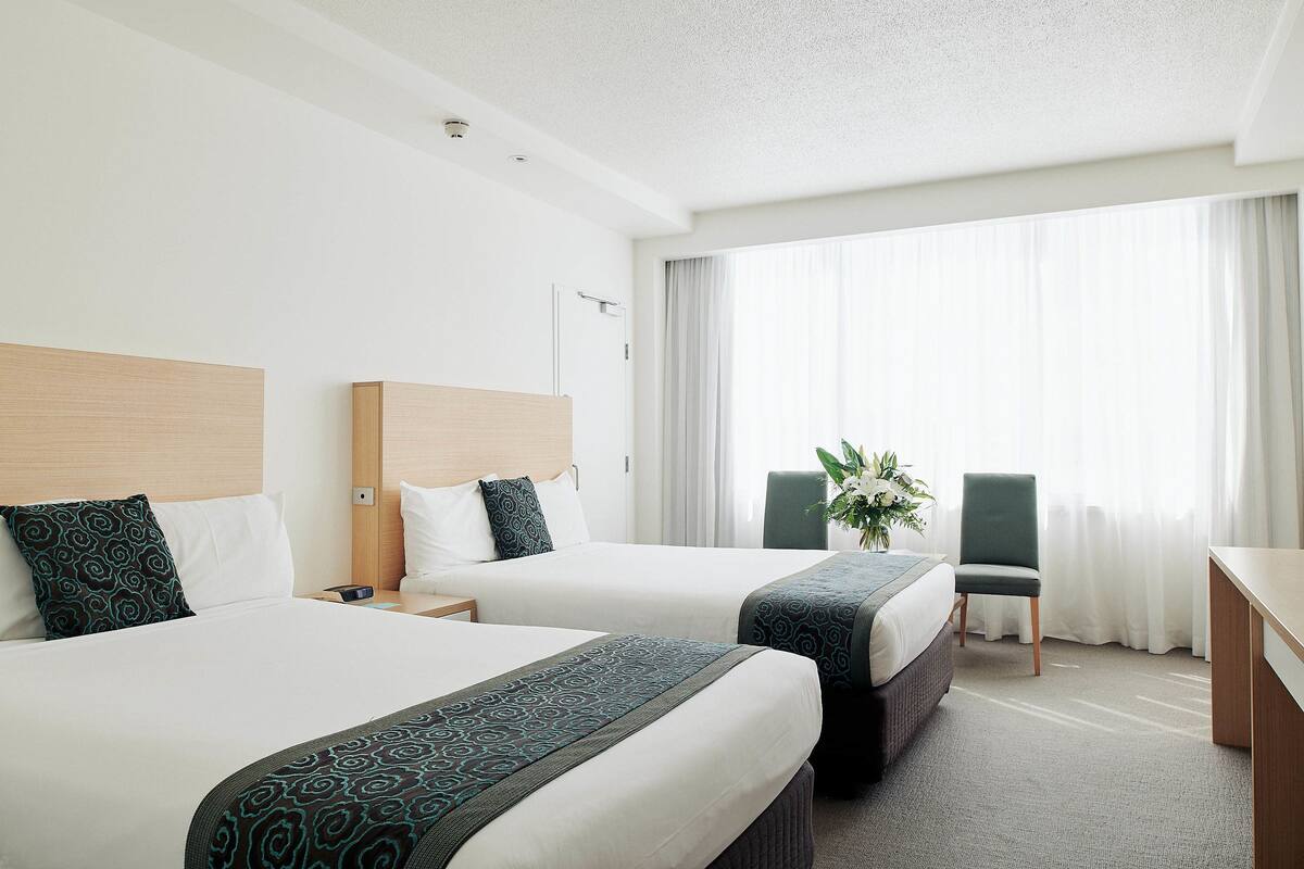 A hotel room with two beds, a desk, a chair, and a large window with curtains.