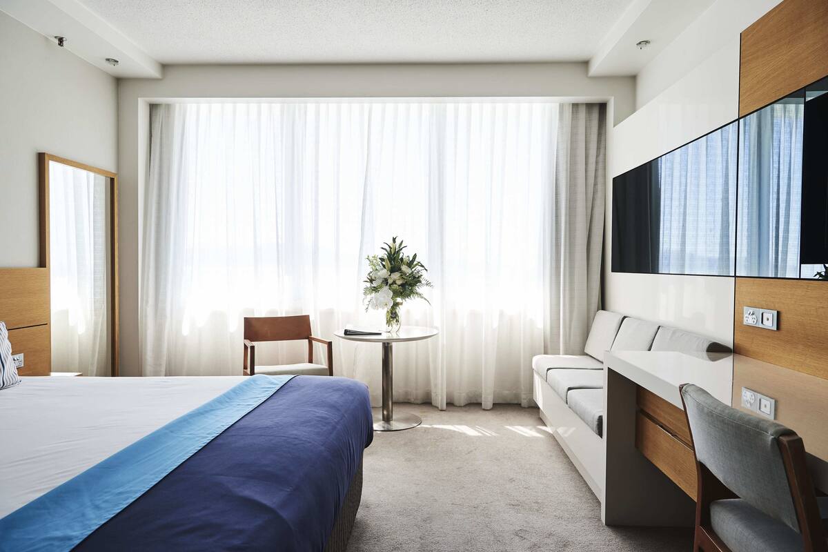 A hotel room with a bed, a desk, a chair, a sofa, a TV, and a window with curtains.
