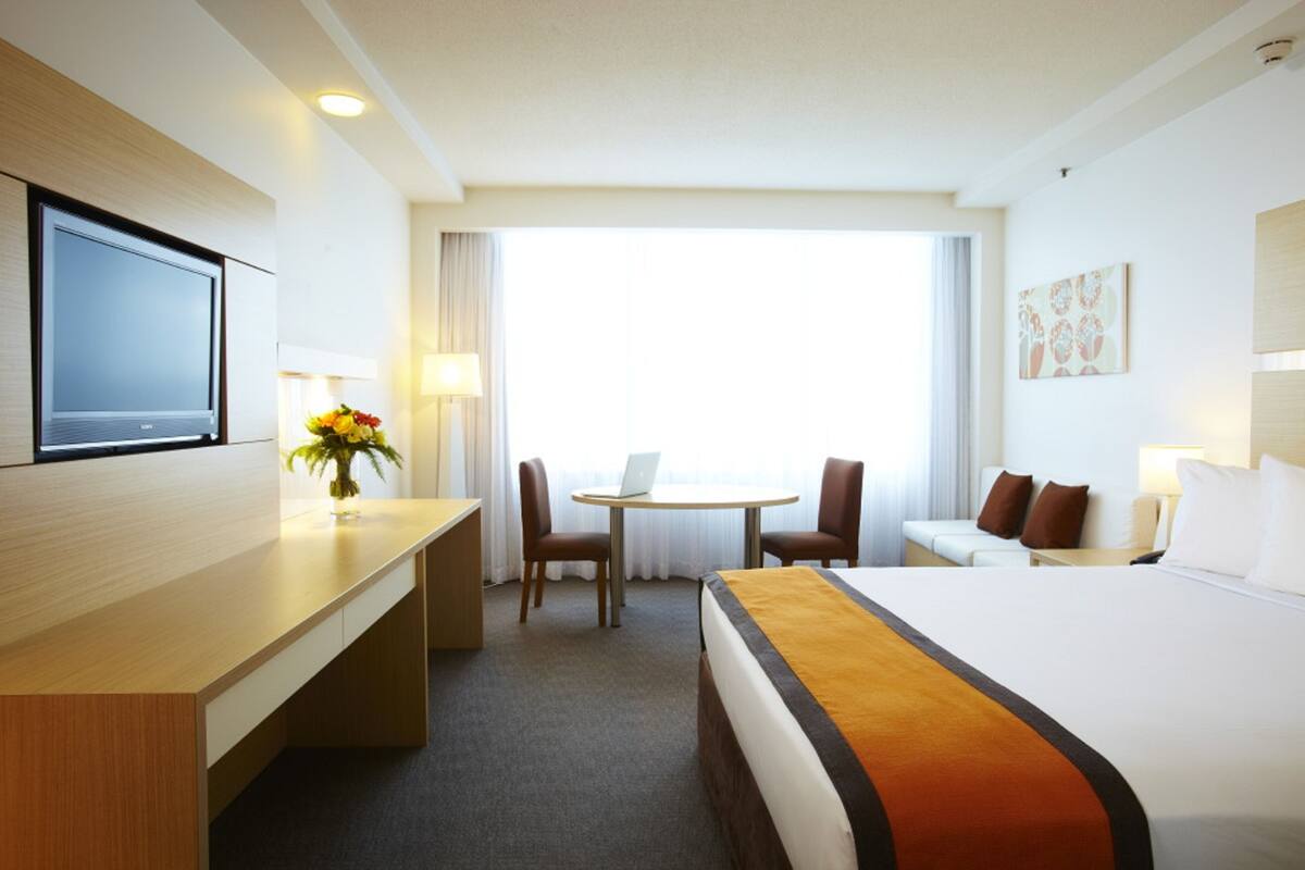 A hotel room with a bed, desk, chair, and a TV.