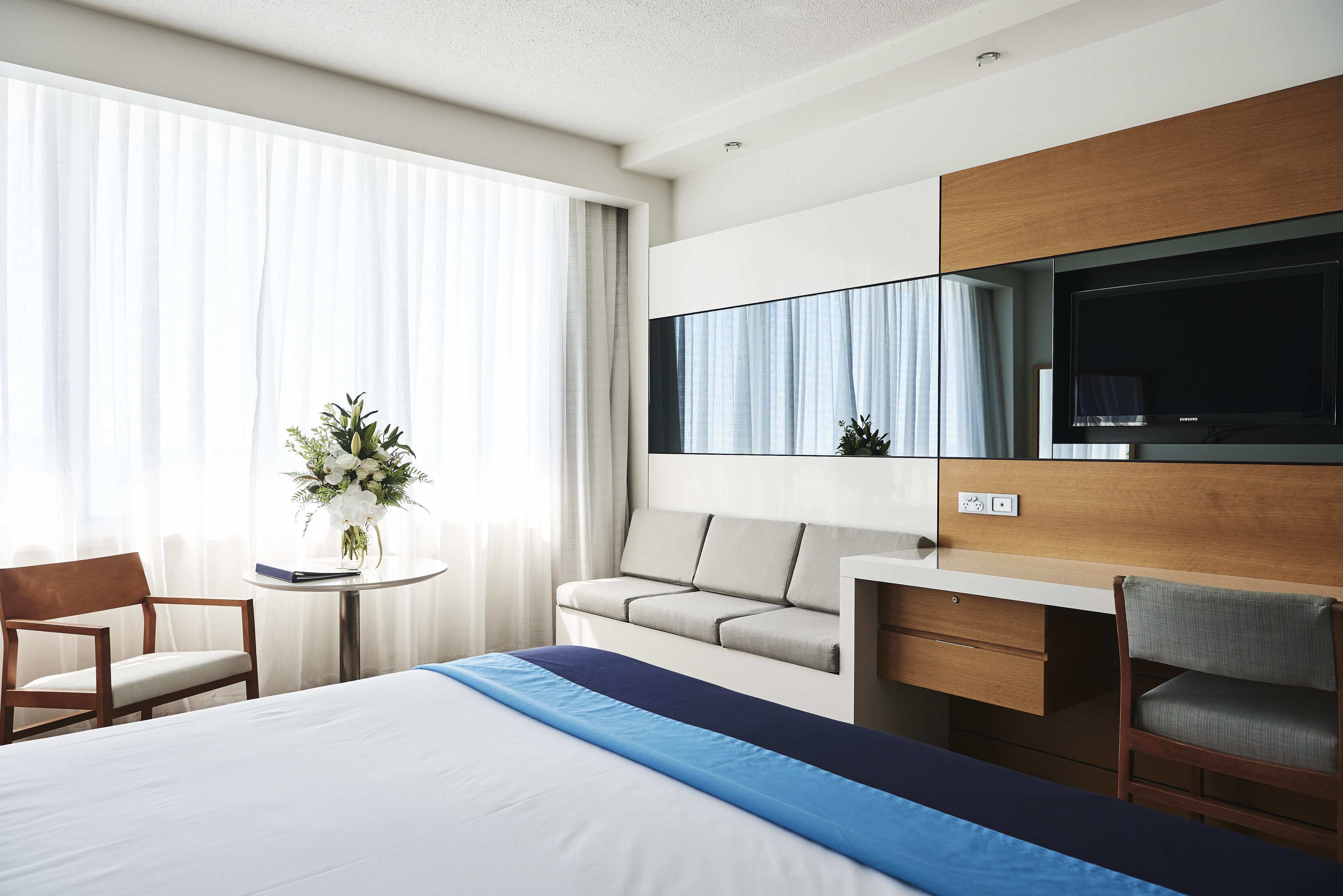 A hotel room with a bed, a desk, a chair, a sofa, a TV, and a window with curtains.