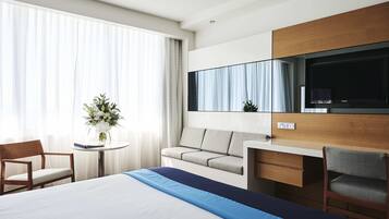 A hotel room with a bed, a desk, a chair, a sofa, a TV, and a window with curtains.