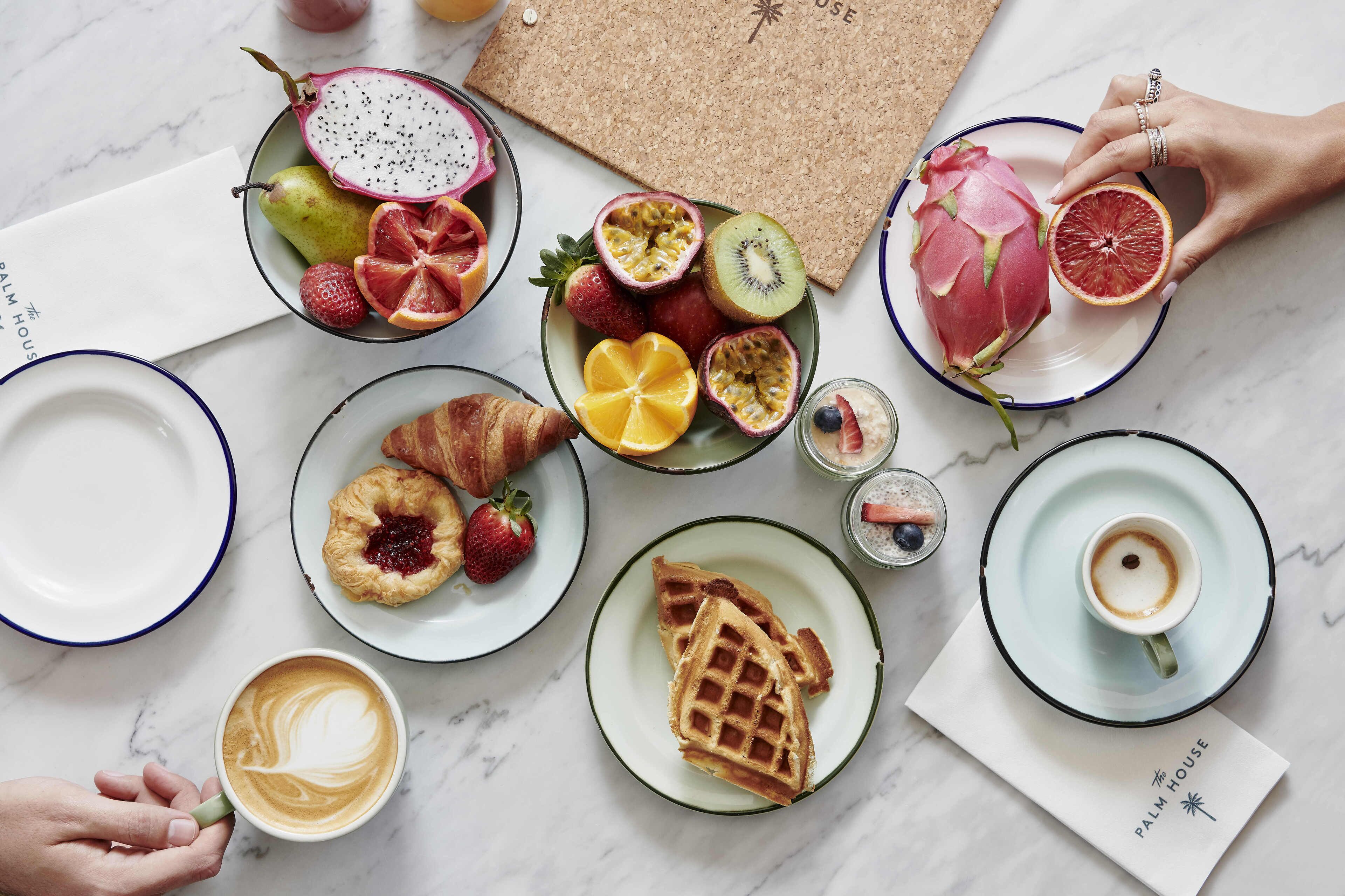 A breakfast setting with various fruits, pastries, and a cup of coffee on a marble table.
