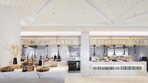 A modern kitchen with marble countertops, a central island with food displays, pendant lighting, and a high ceiling with exposed beams.