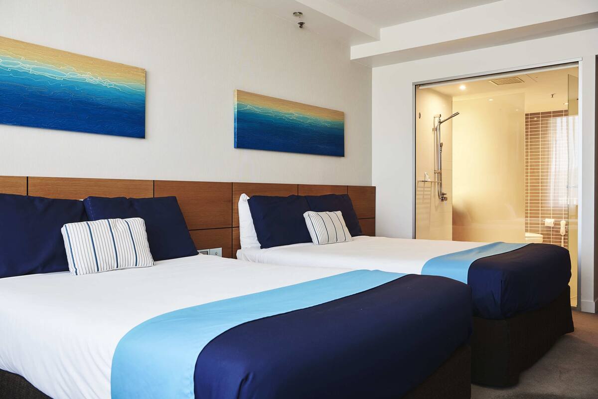 A hotel room with two beds, a wooden headboard, and a shower area.