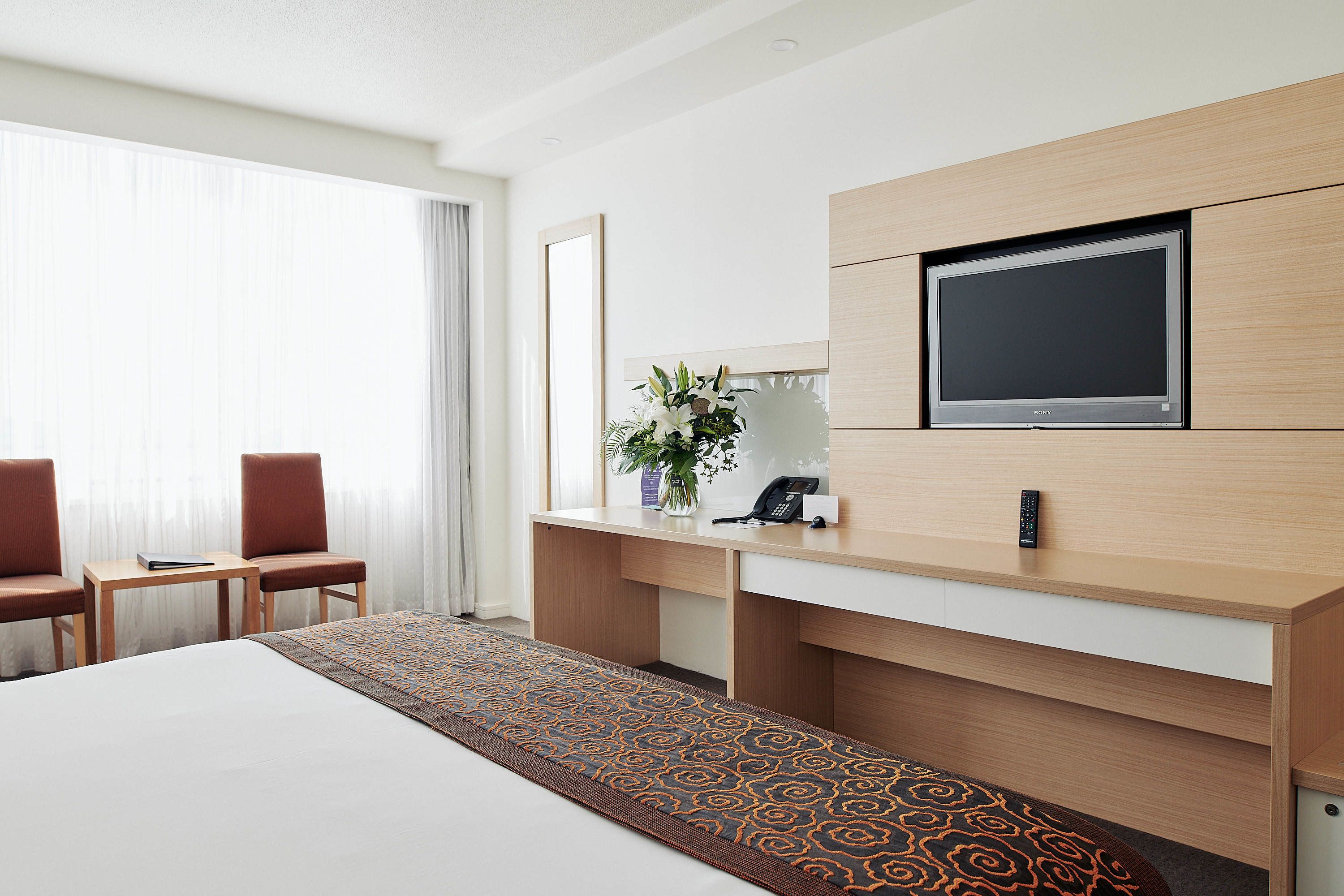 Een hotelkamer met een bed, een bureau met een flatscreen televisie, een telefoon en een vaas met bloemen.