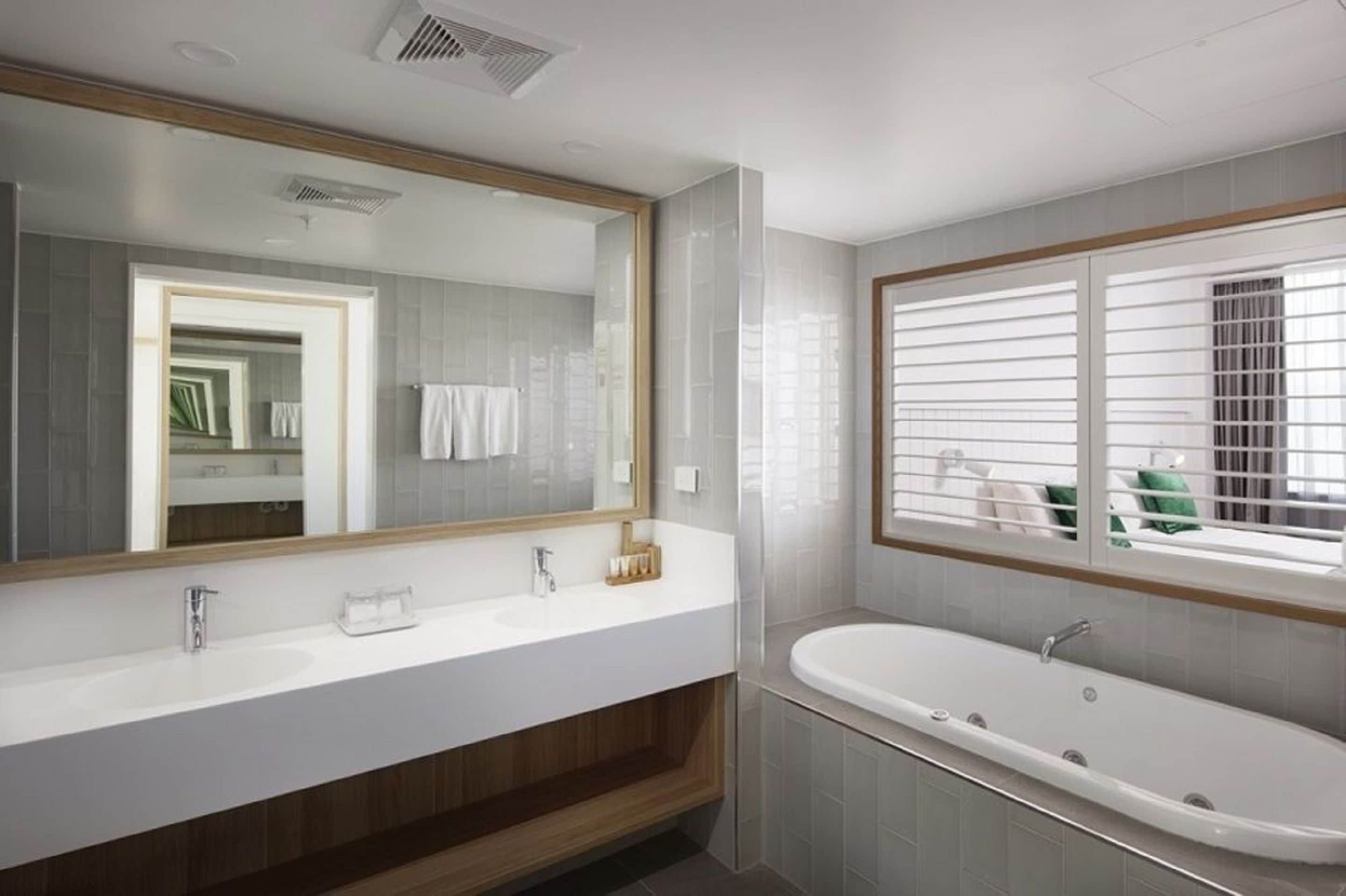 A modern bathroom with a large mirror, two sinks, a bathtub, and a window with blinds.