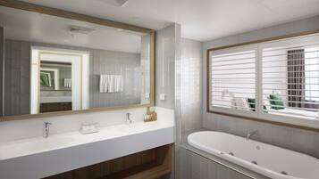 A modern bathroom with a large mirror, two sinks, a bathtub, and a window with blinds.