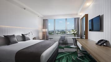 Une chambre d’hôtel moderne dotée d’un grand lit, d’un bureau, d’une chaise, d’un téléviseur à écran plat et offrant une vue sur la ville.