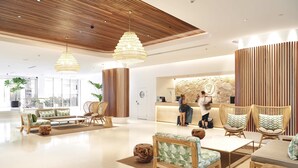 A spacious lobby with wooden ceiling panels, wicker furniture, and a reception desk with a stone wall backdrop.