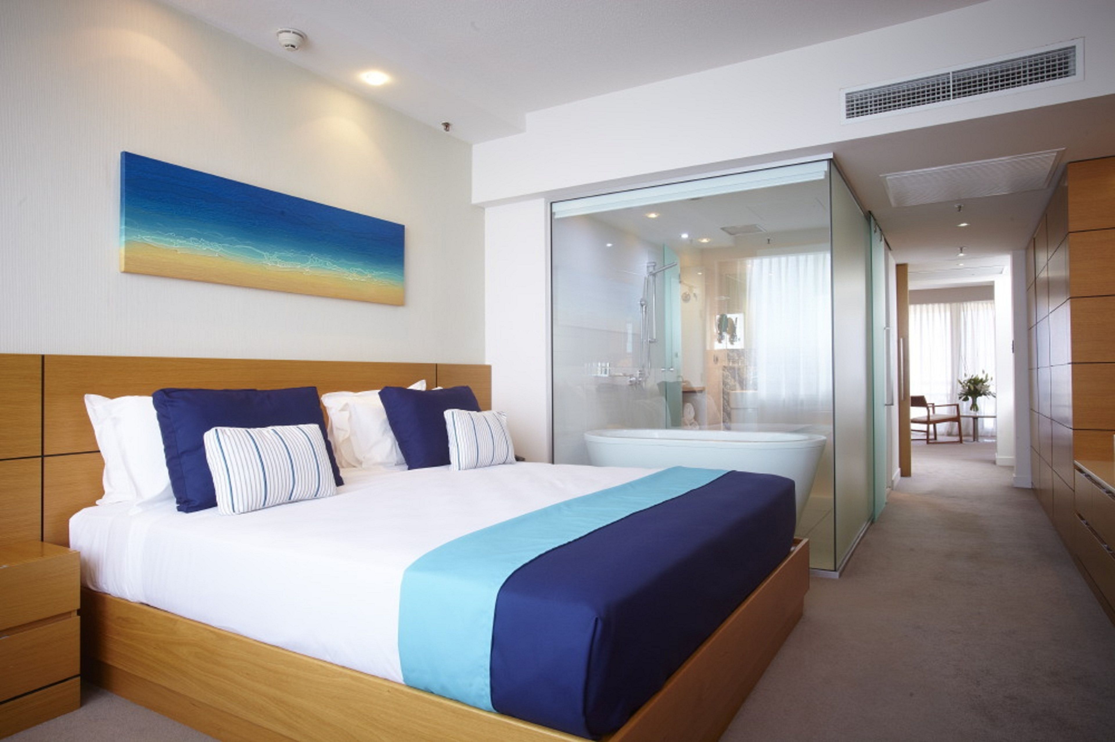 A modern hotel room with a wooden bed, a large window, and a bathroom with a glass partition.