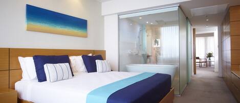 A modern hotel room with a wooden bed, a large window, and a bathroom with a glass partition.