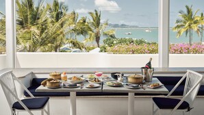 A dining table with various dishes and drinks, overlooking a scenic view of palm trees and the ocean.