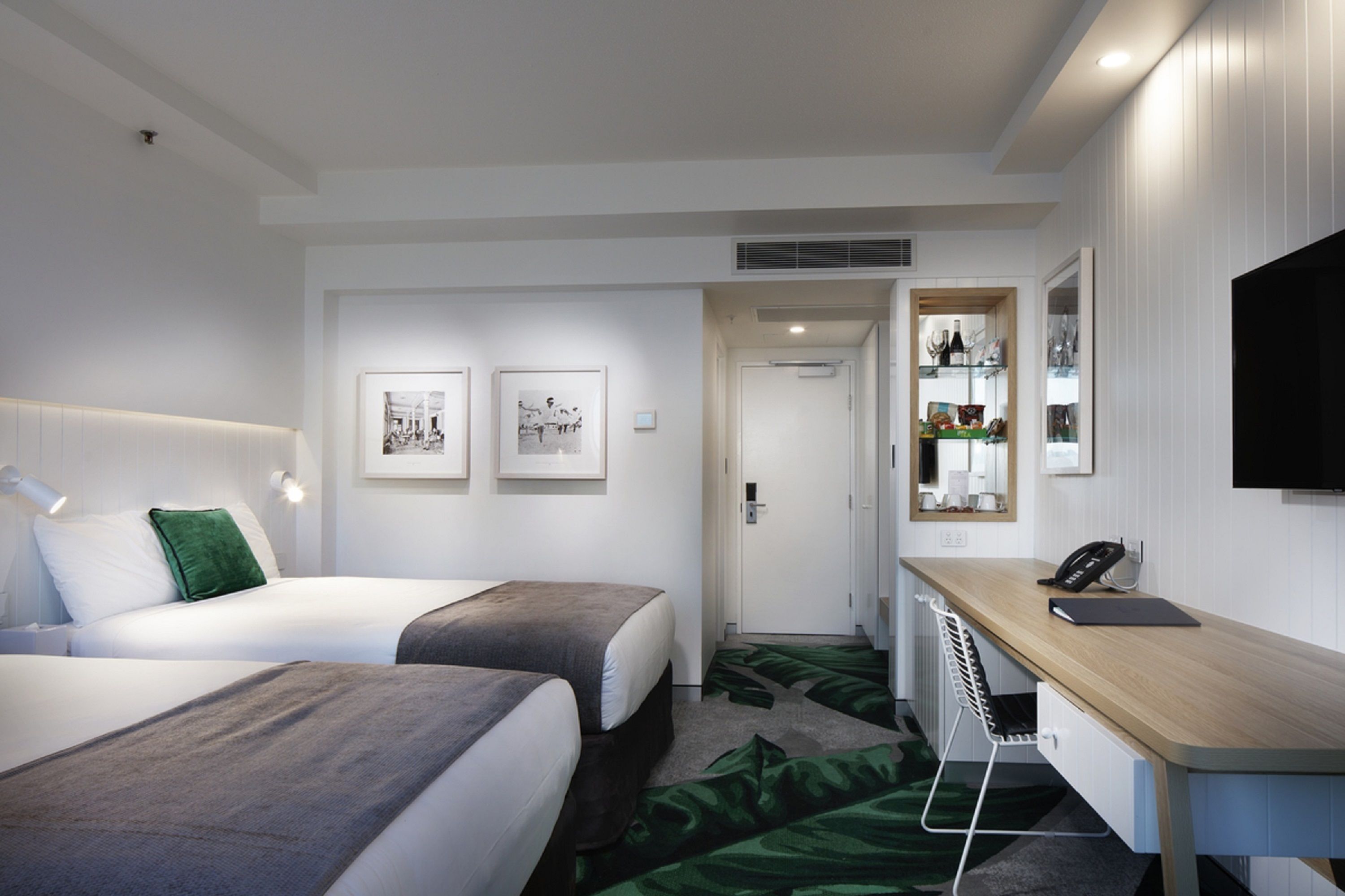 A hotel room with two beds, a desk, a TV, and a small kitchenette.