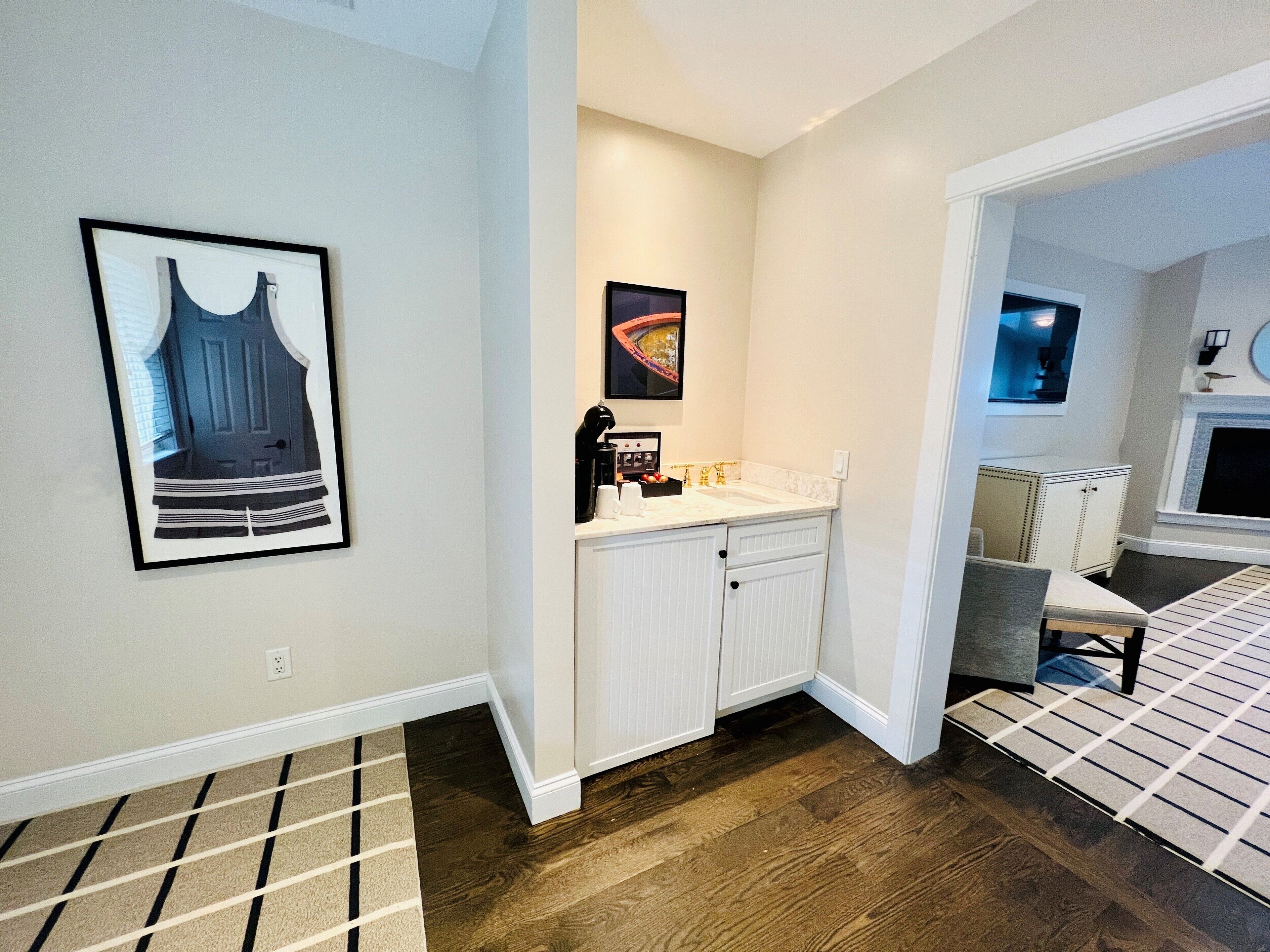 Een moderne badkamer met een witte wastafel, een koffiezetapparaat en een ingelijst schilderij aan de muur.