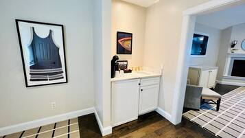 Een moderne badkamer met een witte wastafel, een koffiezetapparaat en een ingelijst schilderij aan de muur.