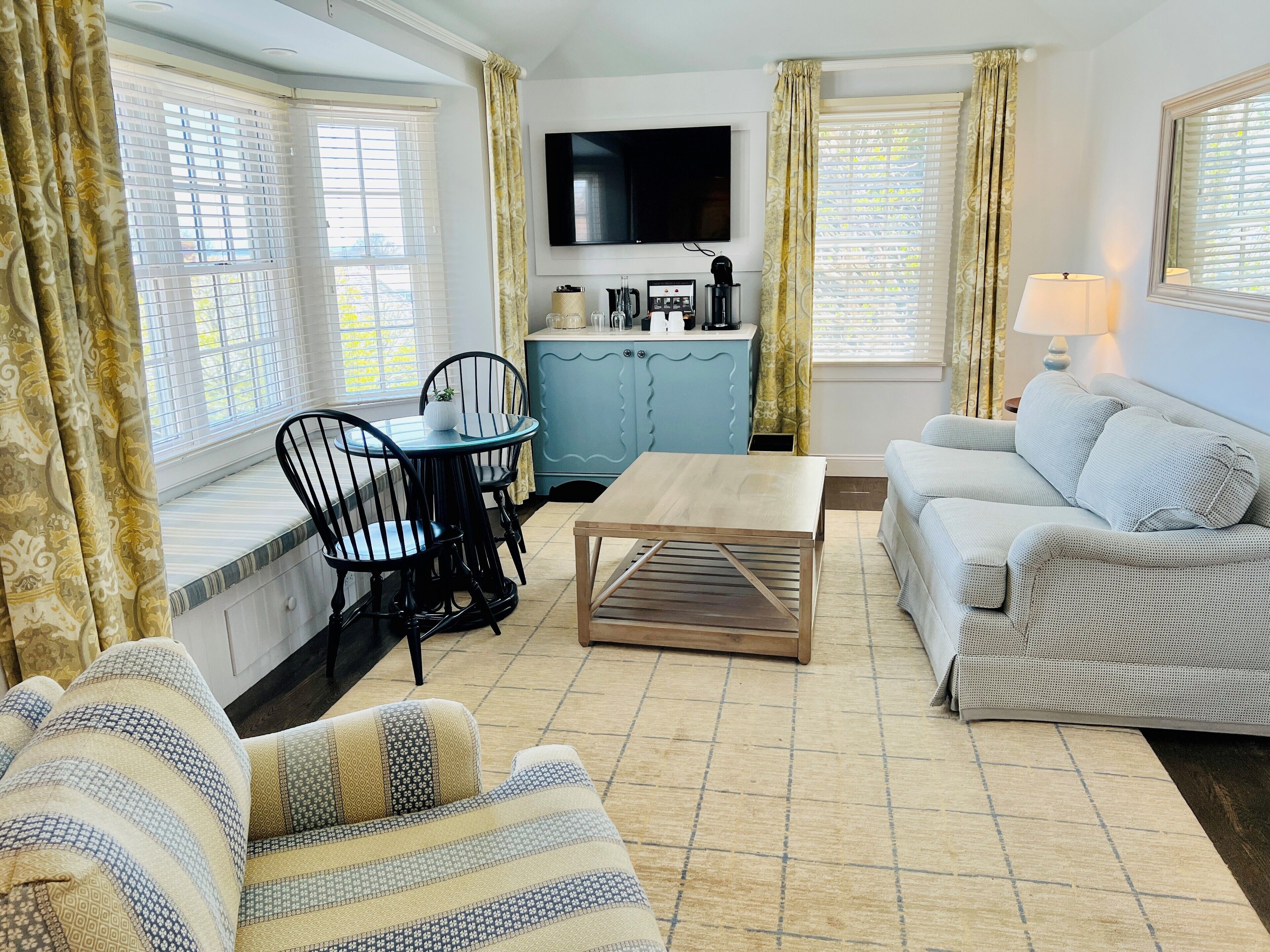 A cozy living room with a sofa, a coffee table, a dining table with chairs, and a television mounted on the wall.