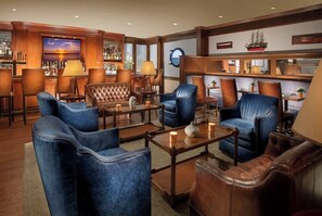 A bar area with leather chairs, a television displaying a sunset, and a ship model on the wall.