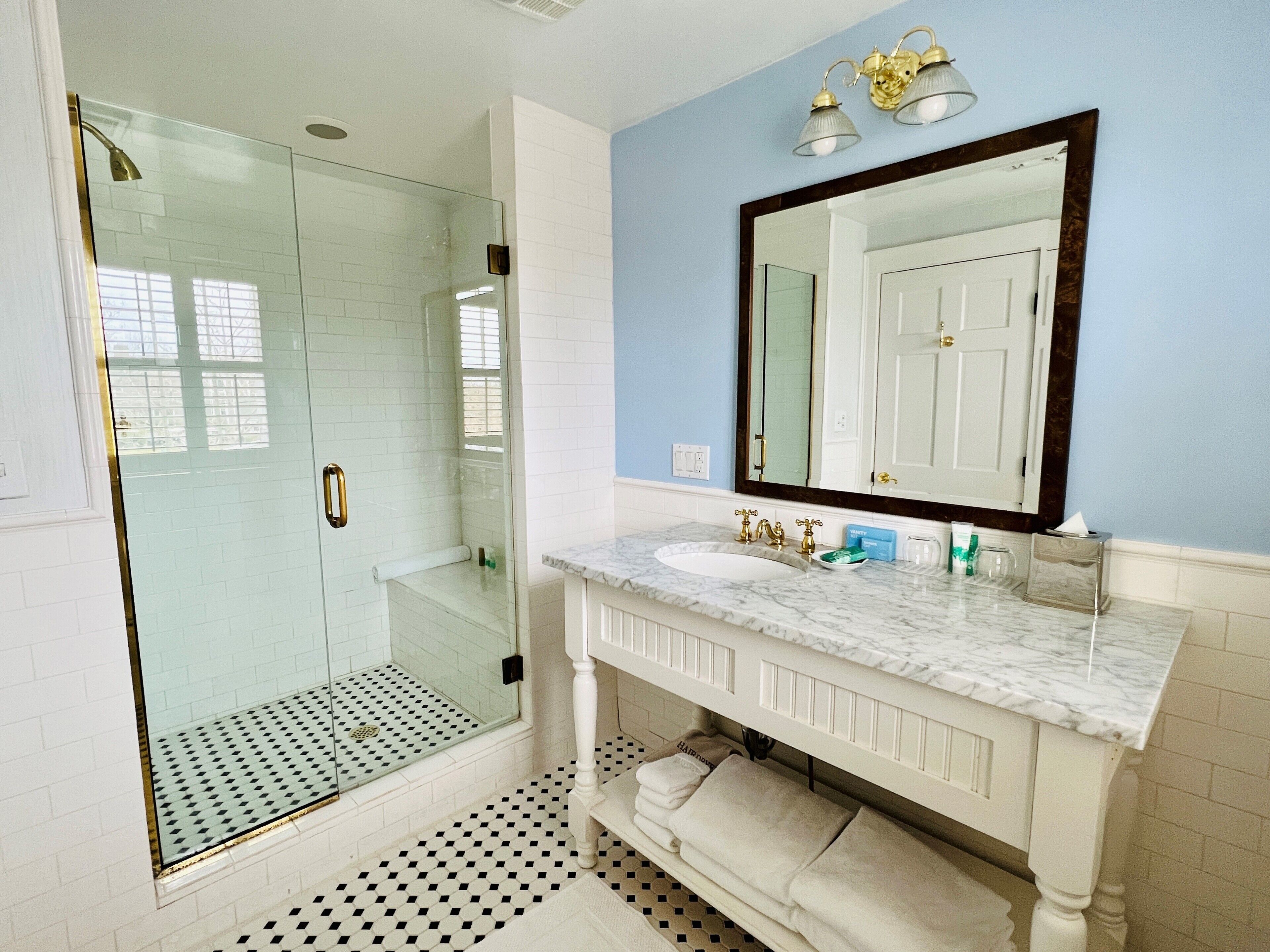 Une salle de bain dotée d’une douche à parois de verre, d’un lavabo en marbre et d’un grand miroir au-dessus du meuble-lavabo.
