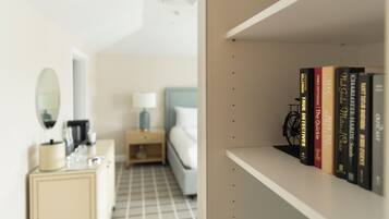 A hotel room with a bed, a nightstand with a lamp, a dresser, and a bookshelf with books.