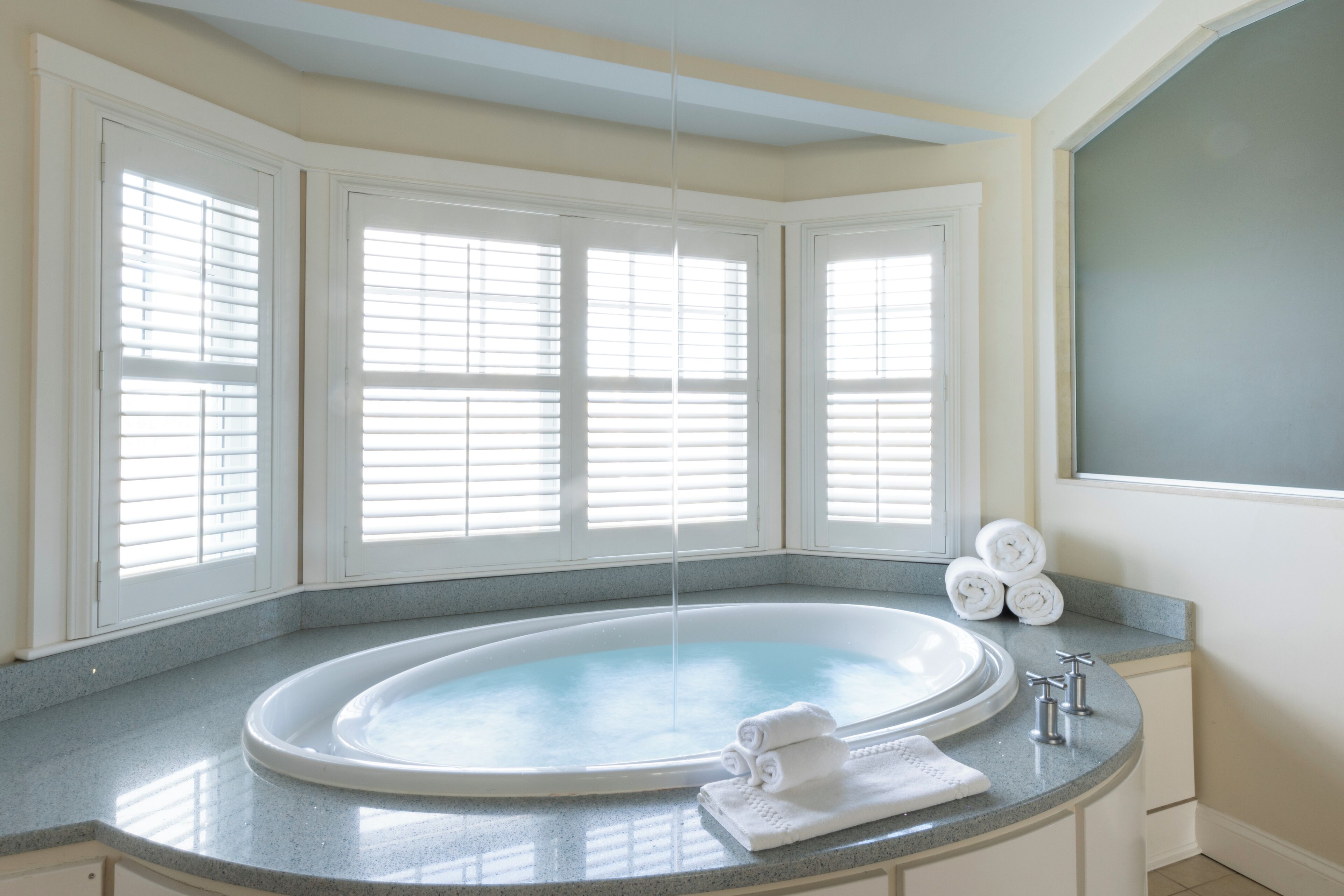 A bathroom with a freestanding bathtub, a sink, and a window with blinds.