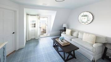 A room with a light-colored sofa, a small round table, a coffee table with a tray, a mirror on the wall, and a door leading to an outdoor area.