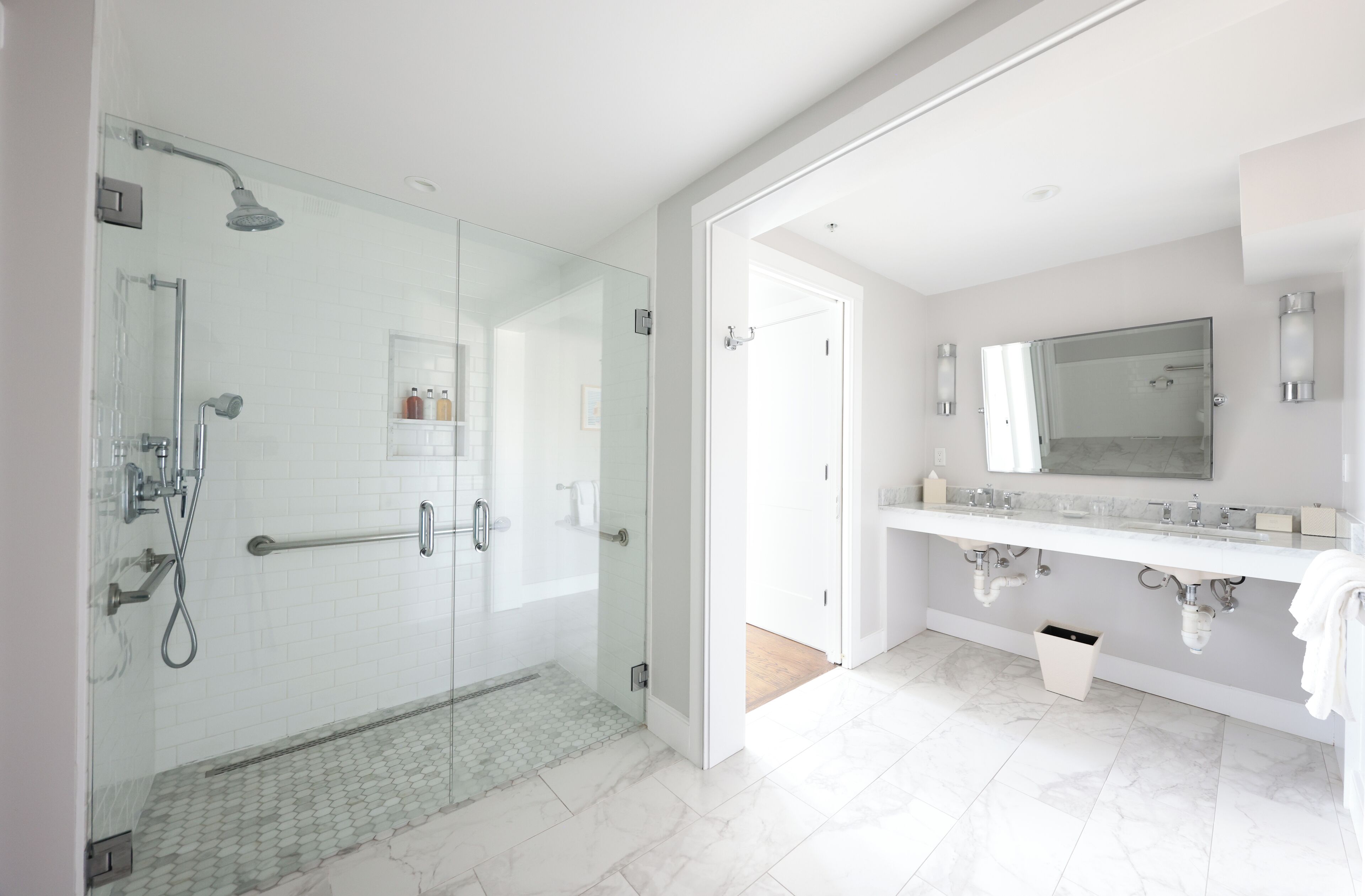 A modern bathroom with a glass-enclosed shower, a white vanity with a large mirror, and a tiled floor.