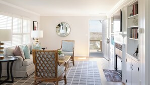 A living room with a sofa, chairs, a coffee table, a side table with a lamp, a large mirror, and a bookshelf.