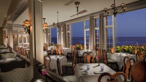 A restaurant with tables and chairs, large windows, and a view of the ocean.