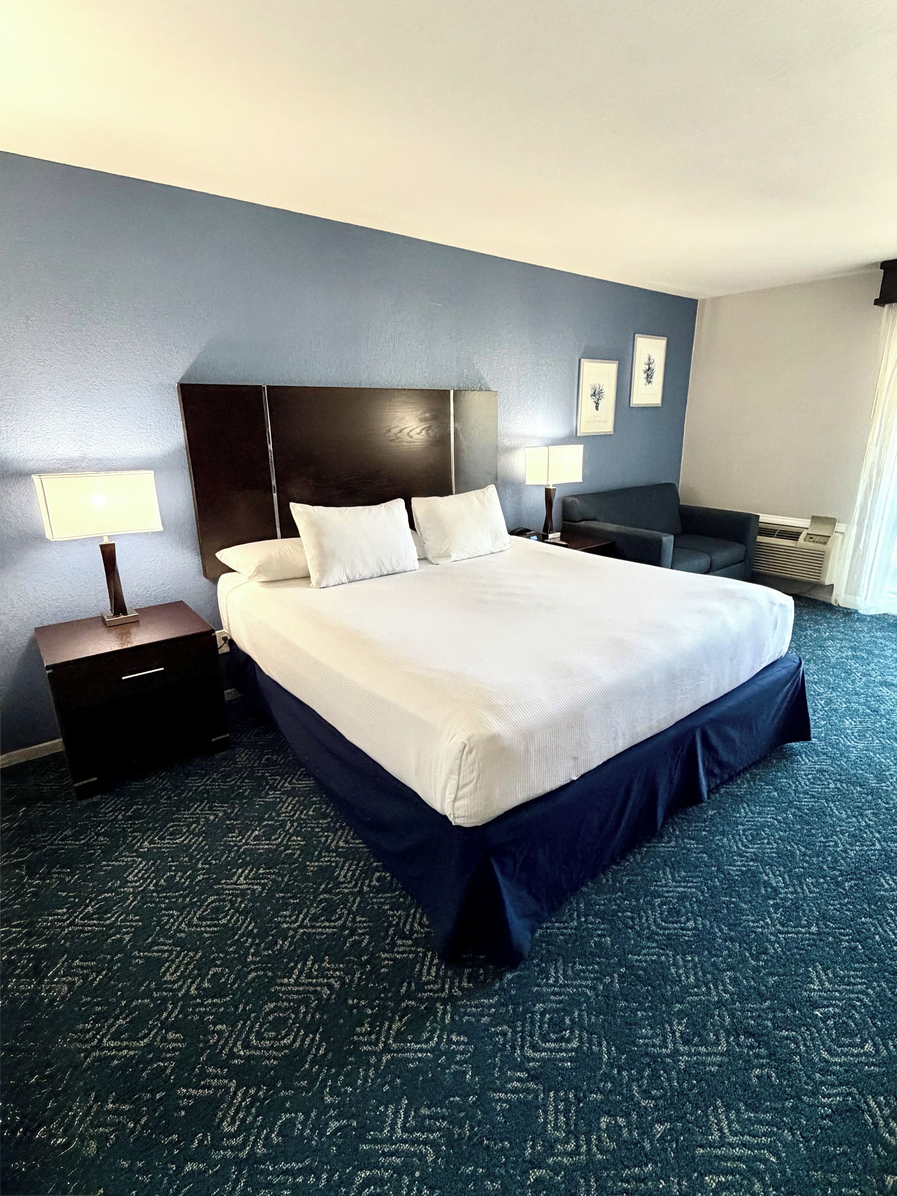 A hotel room with a large bed, two bedside tables, a dark headboard, and a patterned carpet.