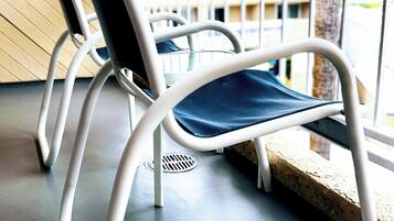 A chair with a metal frame and a dark cushion, positioned on a balcony with a view of buildings and a tree.