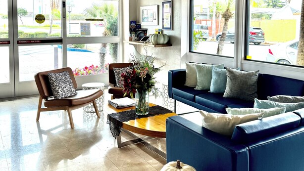 A modern lobby with a blue sofa, a wooden chair, a coffee table, and a decorative white pumpkin. - The Pacific Inn (Seal Beach)