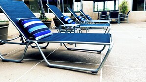 A row of sun loungers with striped cushions, arranged on a tiled patio with a building in the background. - The Pacific Inn (Seal Beach)