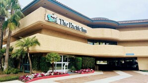 A hotel named "The Pacific Inn" with a curved facade, palm trees, and a landscaped entrance. - The Pacific Inn (Seal Beach)