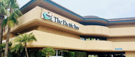 A hotel named "The Pacific Inn" with a curved facade, palm trees, and a landscaped entrance.