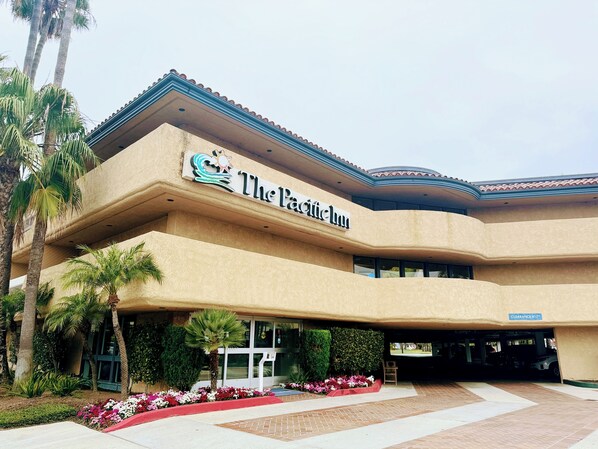 A hotel named "The Pacific Inn" with a curved facade, palm trees, and a landscaped entrance. - The Pacific Inn (Seal Beach)