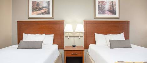 A hotel room with two beds, a nightstand with lamps, and framed pictures on the wall.