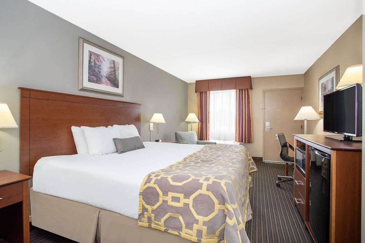 Een hotelkamer met een groot bed, twee nachtkastjes, een bureau met stoel, een televisie en een raam met gordijnen.
